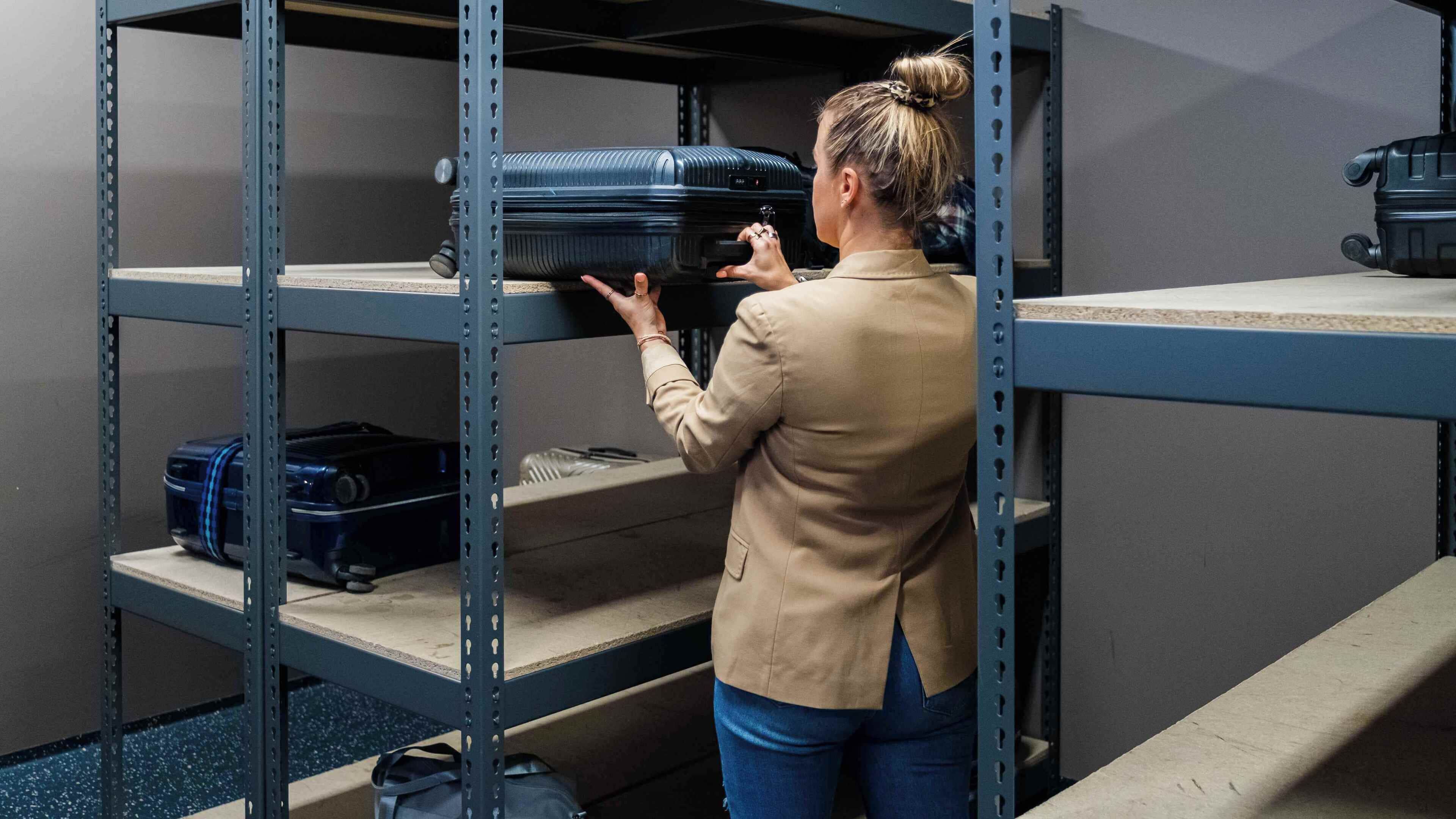 A person organizing luggage on metal shelves in a storage area.