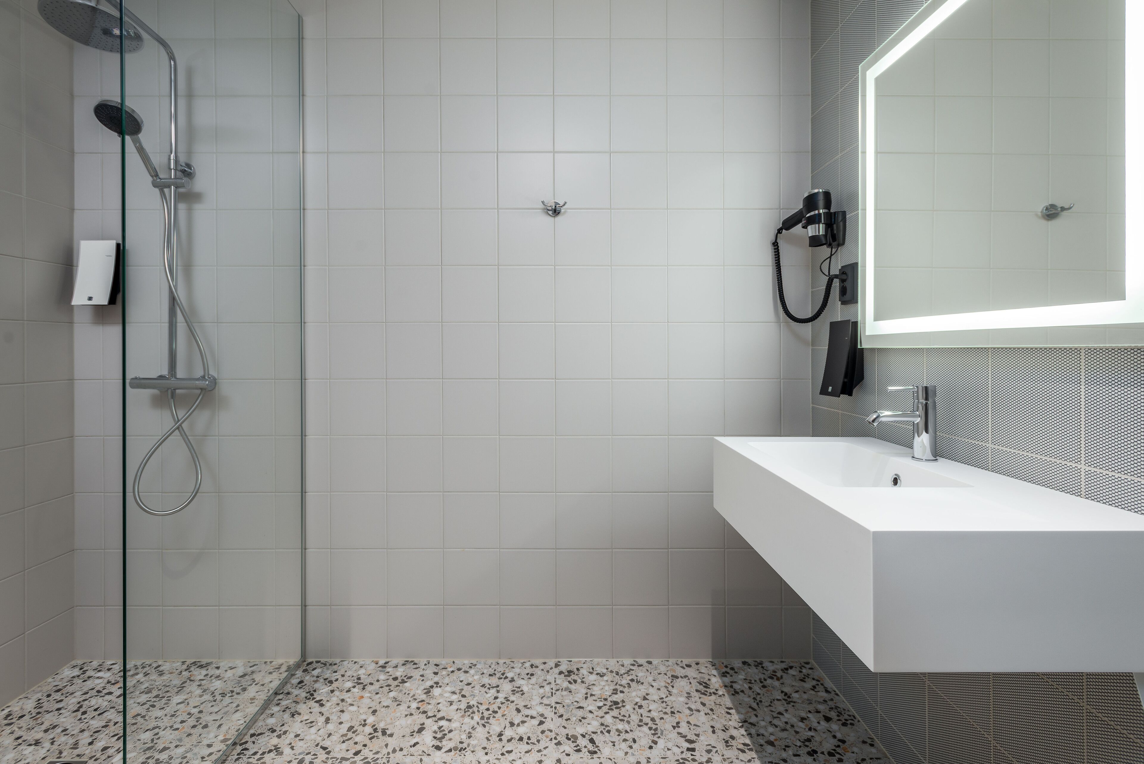A modern bathroom with a glass shower enclosure, a white sink, and a mirror with a lighted frame.