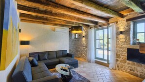 A modern living room with a sectional sofa, a glass coffee table, and a stone wall. - Cozy home in Rakotule (Rakotule)