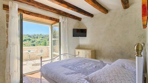 A bedroom with a bed, a television, and a balcony with a table and chair. - Cozy home in Rakotule (Rakotule)