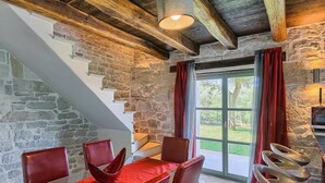 A dining area with a stone wall, wooden beams, and a view of a garden through a glass door. - Cozy home in Rakotule (Rakotule)