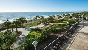 A beachfront promenade with a row of sun loungers, palm trees, and a clear view of the ocean. - Beachside Serendipity Oceanfront 2 Bedroom (Myrtle Beach)