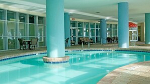 Une piscine intérieure à l’eau d’un bleu cristallin, entourée de piliers bleus et bordée d’une terrasse carrelée.