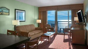Une chambre d’hôtel équipée d’un canapé, de fauteuils, d’une table à manger, d’une télévision et d’un balcon offrant une vue sur l’océan.
