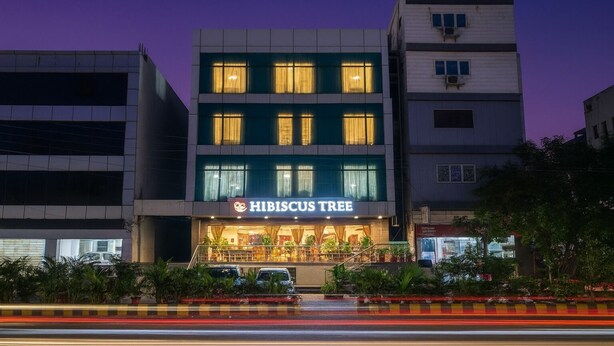 A building with a sign reading "Hibiscus Tree" at the entrance, surrounded by greenery and a road with light trails. - Hotel Hibiscus Tree- Bachupally (Hyderabad)