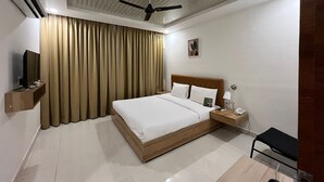A hotel room with a bed, a TV, a ceiling fan, a bedside table with a phone, and a chair. - Hotel Hibiscus Tree- Bachupally (Hyderabad)
