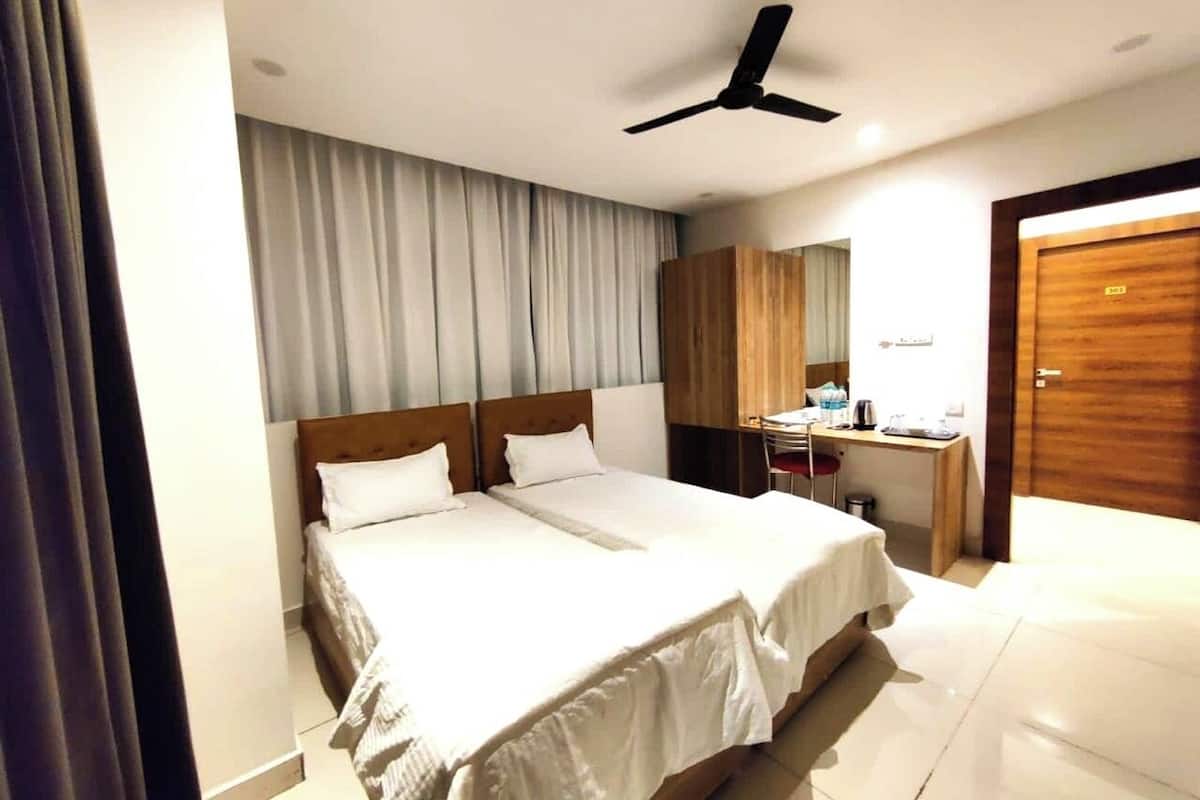 A hotel room with two beds, a desk, a chair, a wardrobe, and a ceiling fan.