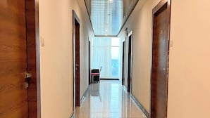 A long, well-lit hallway with wooden doors on both sides, leading to a bright room with a view of the city. - Hotel Hibiscus Tree- Bachupally (Hyderabad)