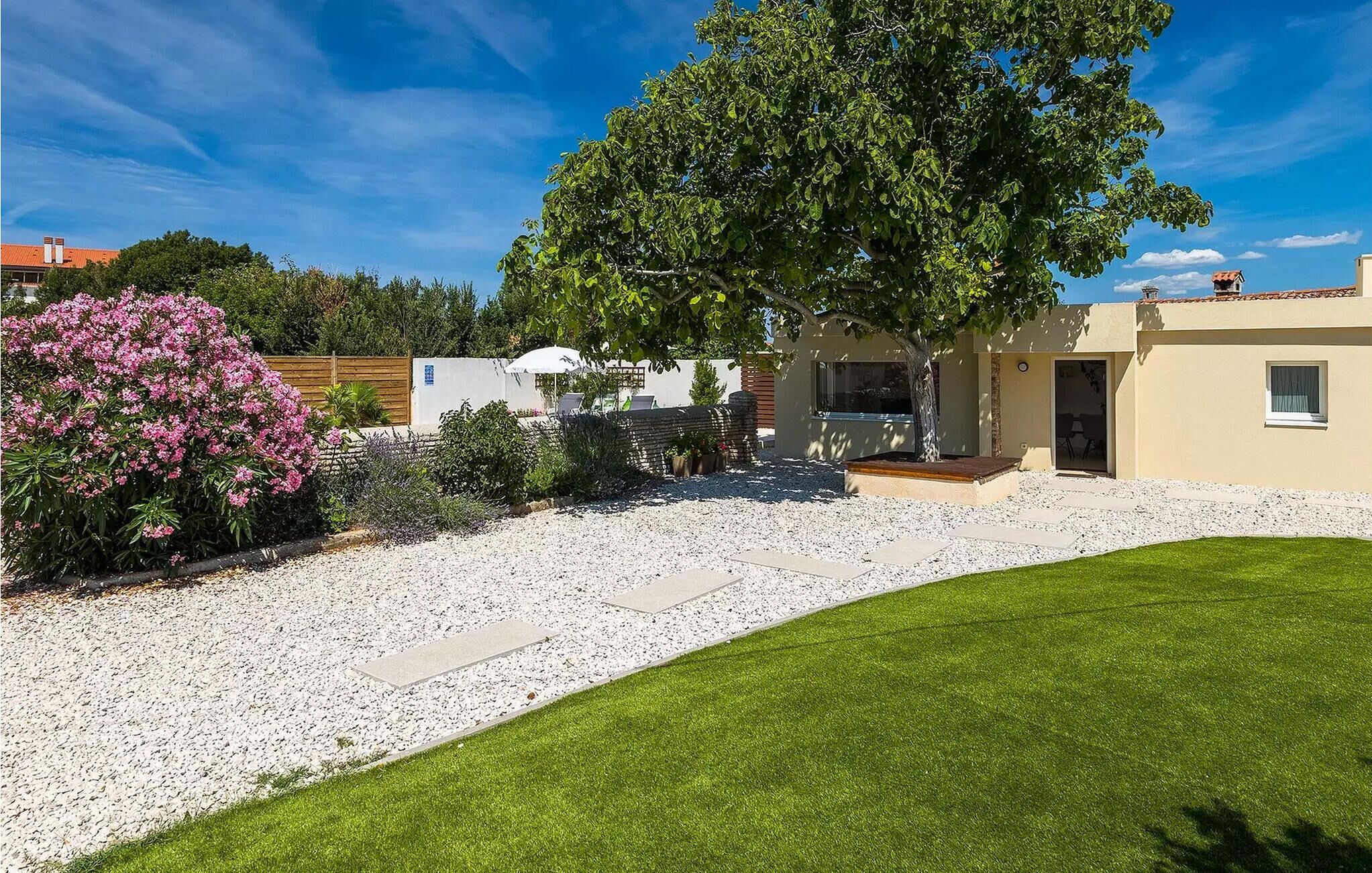 A residential property with a well-maintained lawn, a patio area, and a large tree providing shade.