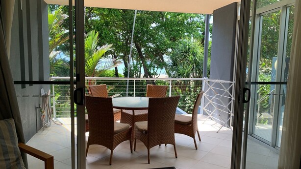 A balcony with a table and chairs, glass doors, and a view of greenery. - BHA 1 Beachfront Haven - 2 bedroom (Mission Beach)