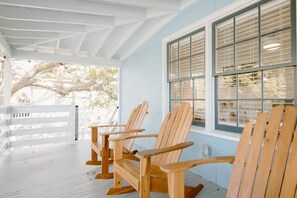Een veranda met houten stoelen en een tafel, een witte balustrade en een raam met luiken.