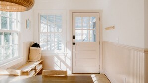 Une pièce lumineuse et blanche, avec un banc en bois, une porte et une fenêtre.
