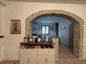 A kitchen with a stone archway, a coffee machine, and a dining area with a sofa. - Casa Celestina (Padenghe sul Garda)