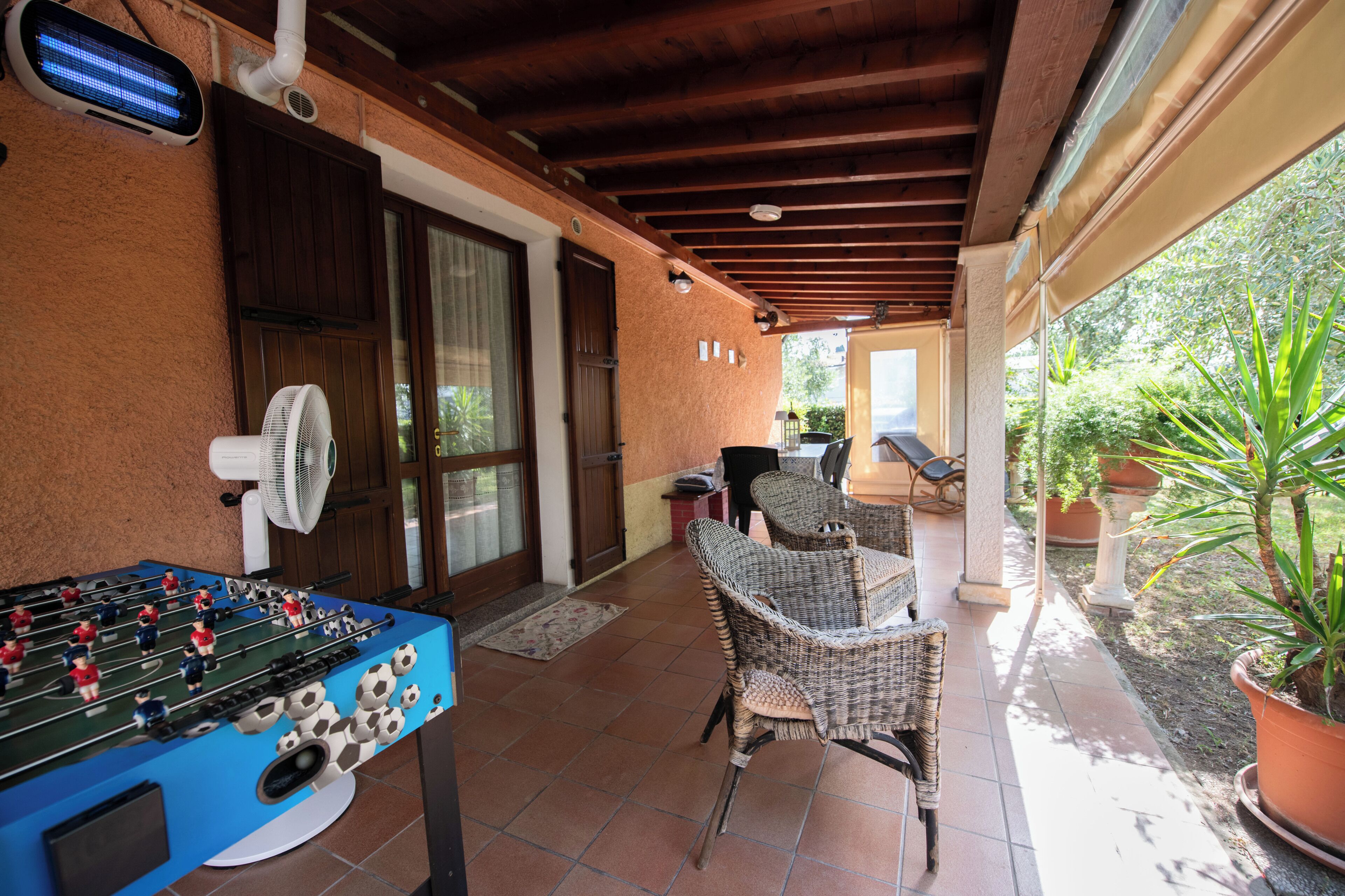 Un patio techado con mesa de fútbol, sillas de mimbre y un ventilador.
