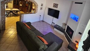 En stue med sofa, fjernsyn, pejs og et spiseområde, som kan anes gennem en bue.