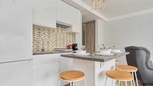 A modern kitchen with white cabinets, a tiled backsplash, a coffee machine, and a bar area with stools. - Stylish Studio in the Center | 15 minutes to the Market Square of Wroclaw (Wroclaw)