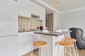 A modern kitchen with white cabinets, a tiled backsplash, a coffee machine, and a bar area with stools.