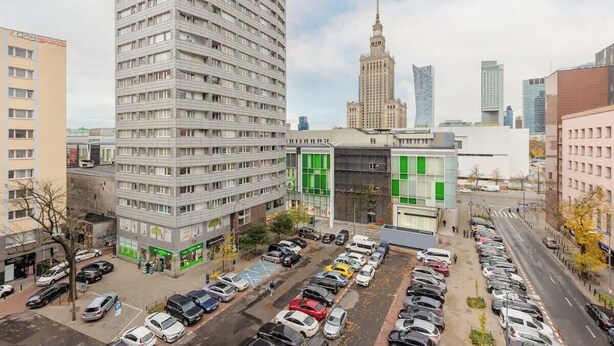 A multi-story parking garage with cars parked in rows, adjacent to a building with a modern facade and green accents.