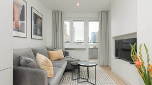 A modern living room with a grey sofa, two black coffee tables, a flat-screen TV, and a large window with curtains.
