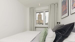 A hotel room with a bed, a window with curtains, and a cityscape view.