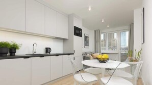 A modern kitchen with white cabinets, a black countertop, and a dining area with a round table and white chairs.