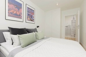 Un dormitorio con cama, almohadas, una lámpara de pared y dos cuadros enmarcados.