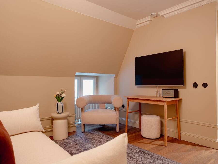 Un dormitorio con cama, una silla, un escritorio, televisor y un radiador.