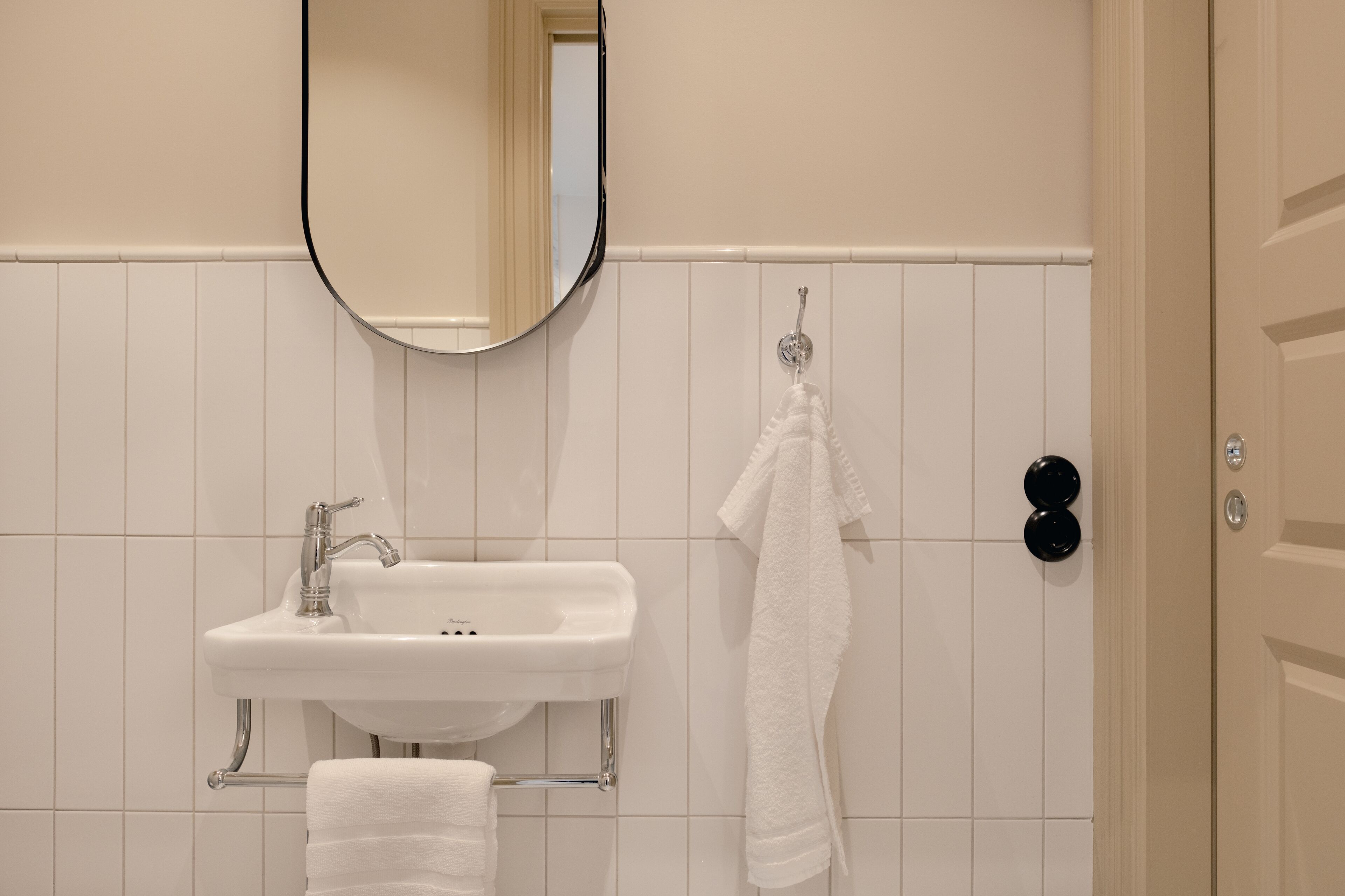 Un baño con lavamanos blanco, un espejo y un perchero para toallas.