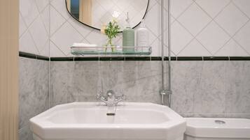 Un baño con un lavabo blanco, una repisa de vidrio con artículos de aseo, y un espejo sobre el lavabo.