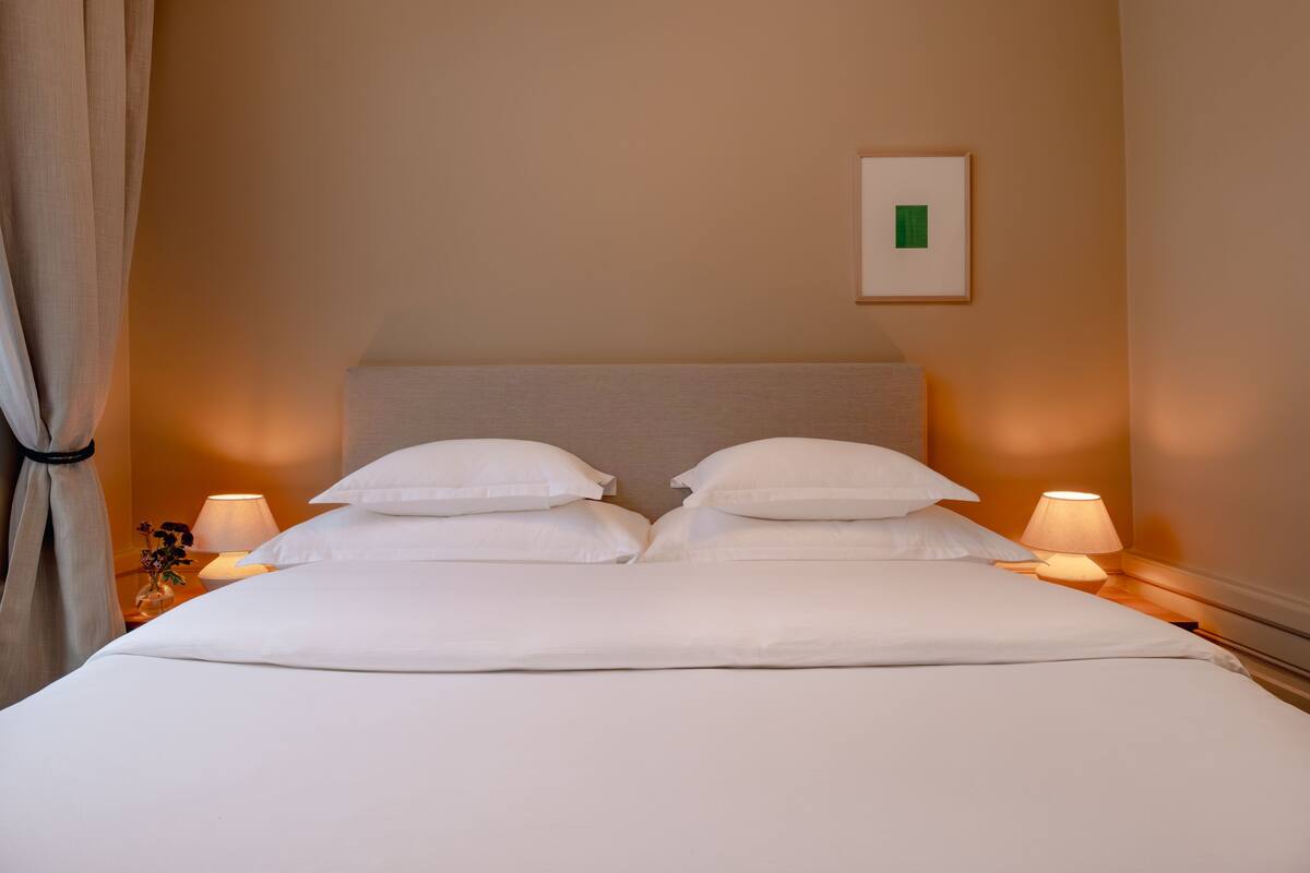 A neatly made bed with white linens and pillows, two bedside lamps, and a framed picture on the wall.