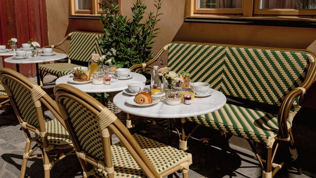 Un comedor con sillas y mesas de mimbre, algunas con platos de comida y bebidas.