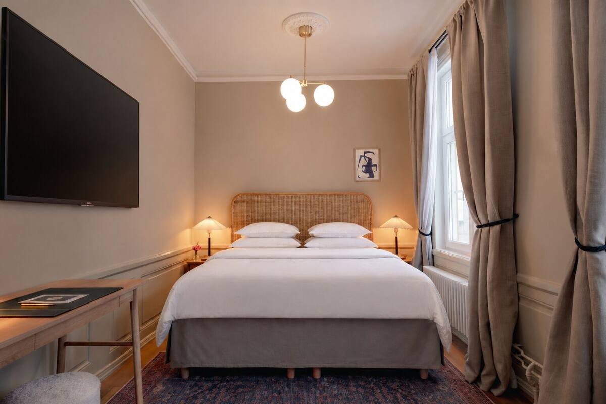 A hotel room with a bed, bedside lamps, a flat-screen TV, and a window with curtains.
