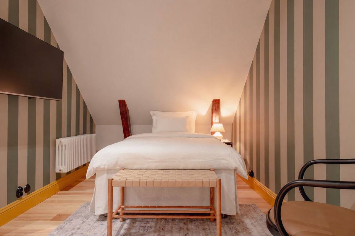 A bedroom with a bed, bedside table, lamp, chair, and a radiator.
