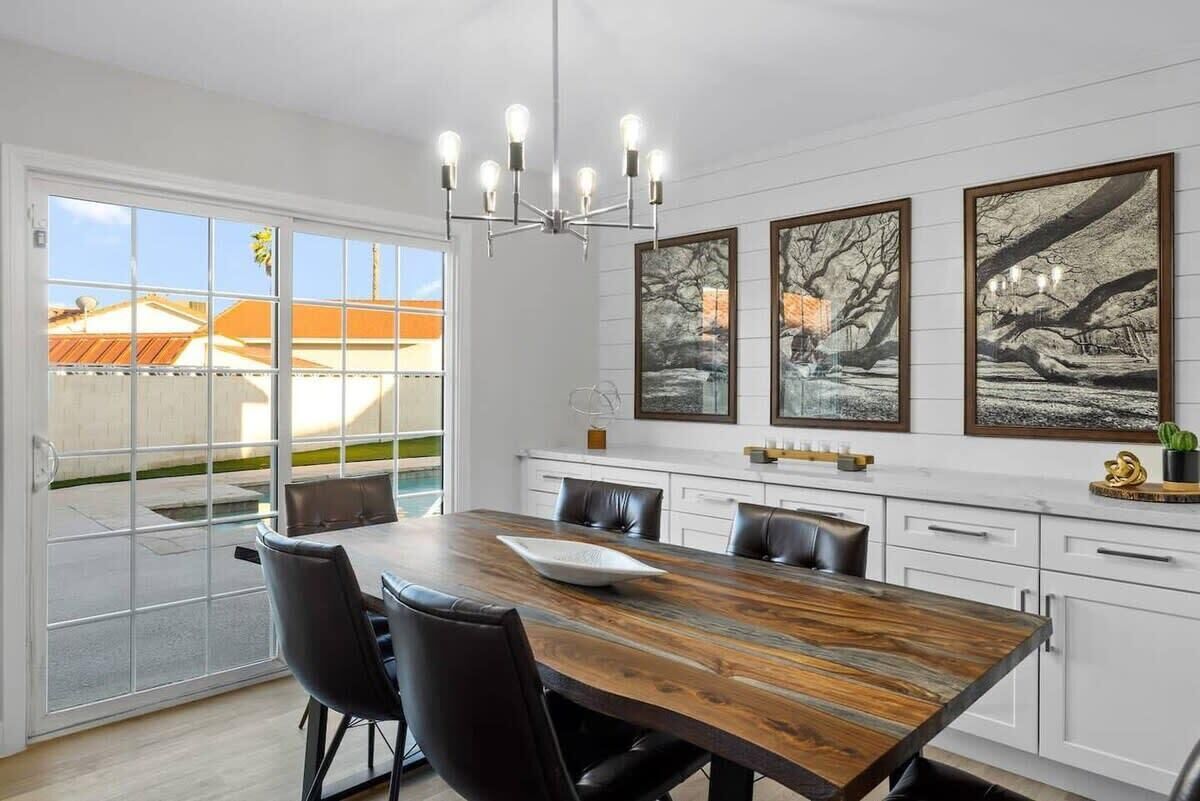 Un coin repas avec une table en bois, des chaises noires, un lustre et des œuvres d’art encadrées accrochées au mur.