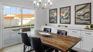 A dining area with a wooden table, black chairs, a chandelier, and framed artwork on the wall. - Single Story 3BR w/ Pool, Hot Tub, Firepit & Grill (Henderson)