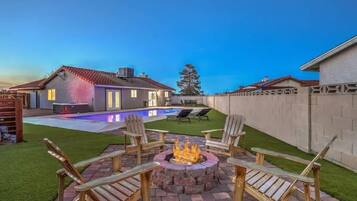 Un jardin avec une piscine, un foyer extérieur et un espace salon aménagé.