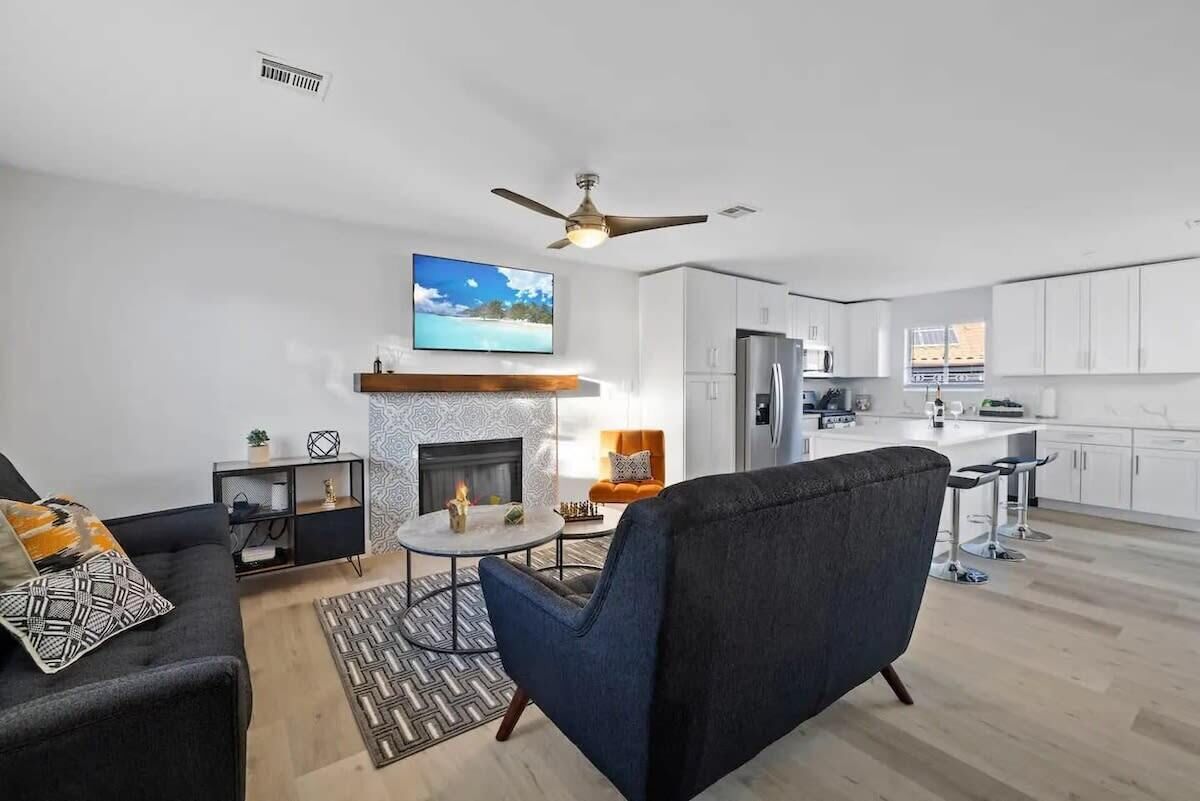 Un salon moderne avec une cheminée, un ventilateur de plafond et une cuisine en arrière-plan.