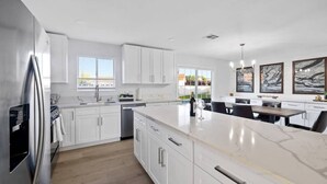A modern kitchen with white cabinets, a marble countertop, and a built-in oven. - Single Story 3BR w/ Pool, Hot Tub, Firepit & Grill (Henderson)