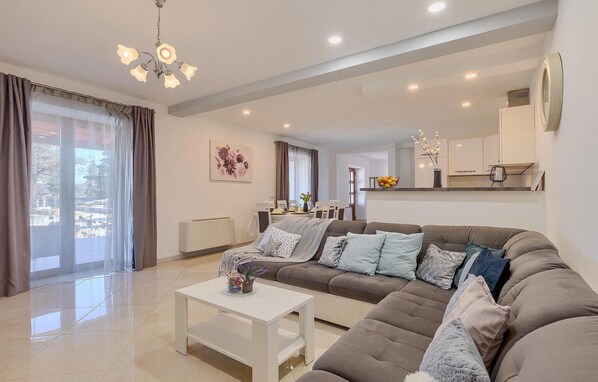 Un salon moderne avec un canapé d’angle, une table basse blanche et un coin repas à l’arrière-plan.