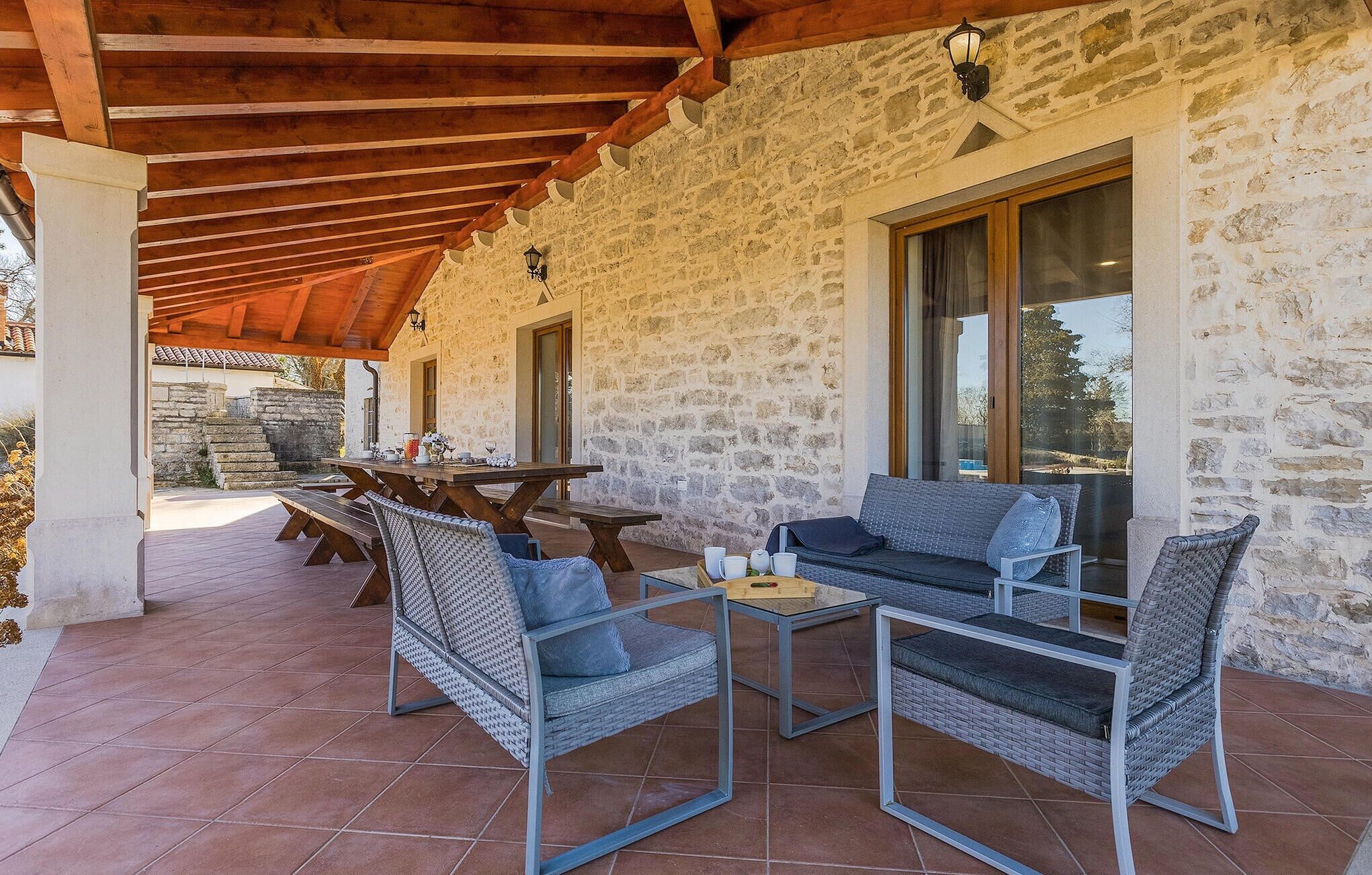 Un área de estar al aire libre techada, con paredes de piedra, vigas de madera y muebles de mimbre.
