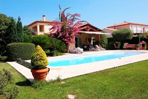 Relax by the pool surrounded by lush greenery and a vibrant pink tree.