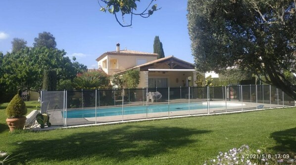 Enjoy a refreshing swim in the pool surrounded by a lush lawn and a charming two-story house.