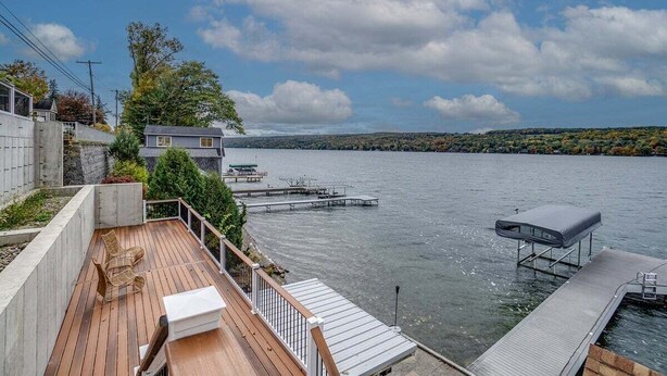 Una terraza de madera con mobiliario exterior, un muelle que se adentra en un lago y una casa al fondo.