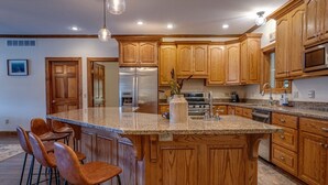 Una cocina con armarios de madera, una isla grande con taburetes de bar, electrodomésticos de acero inoxidable y encimeras de granito.