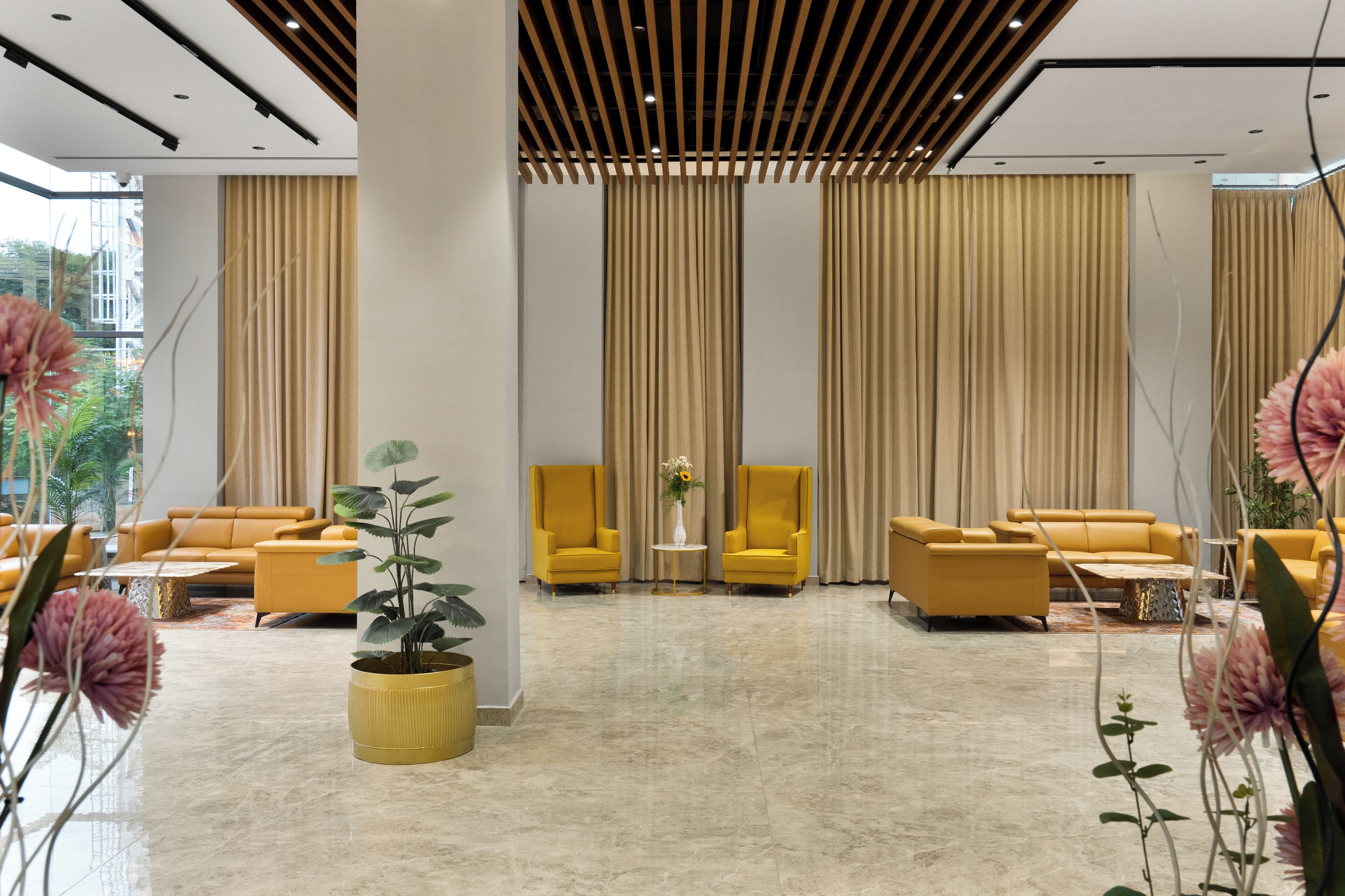 Um hall moderno com poltronas amarelas, uma mesa central com um vaso e uma janela grande com cortinas.