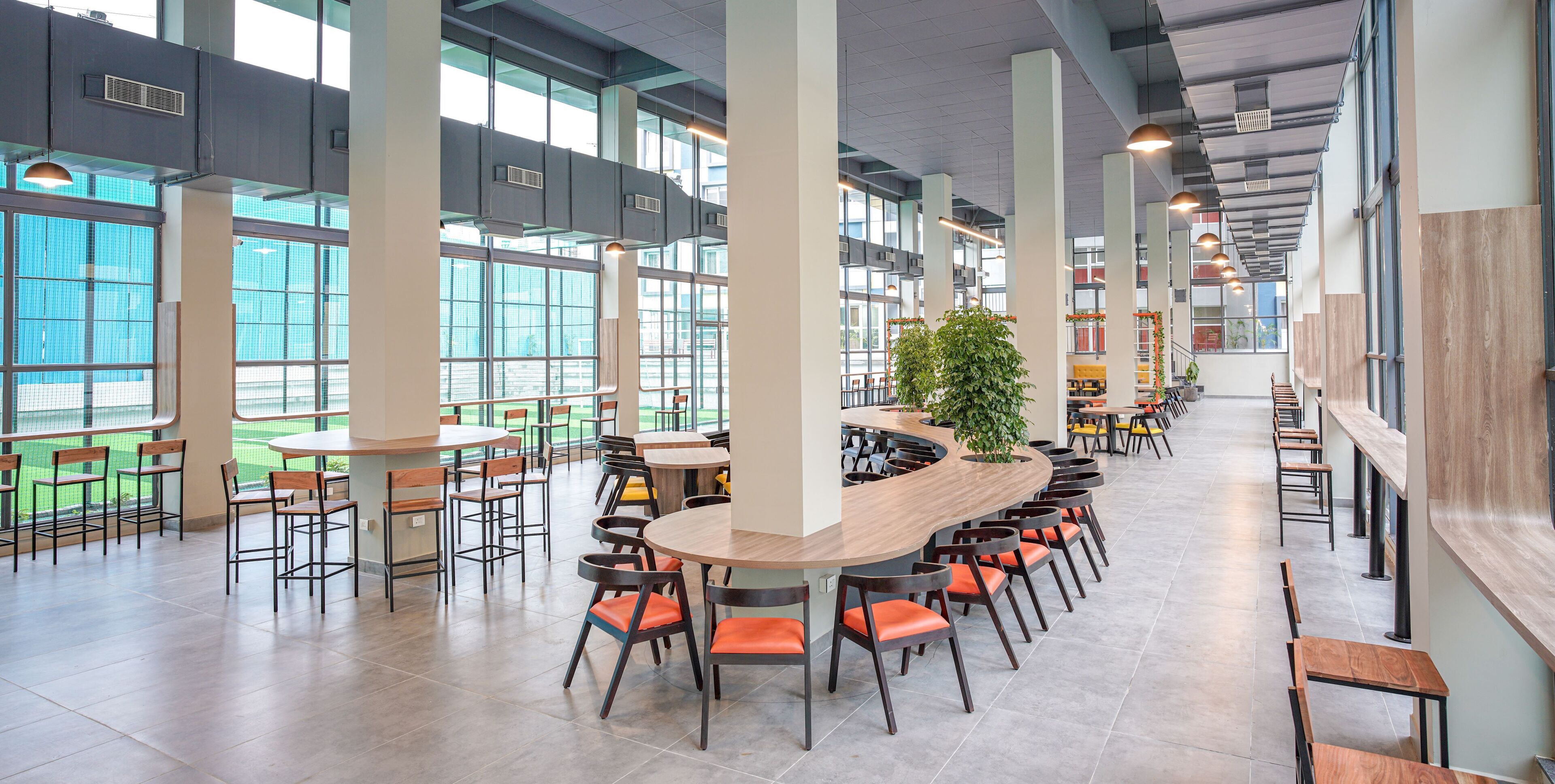 A spacious indoor area with high ceilings, large windows, and multiple seating arrangements including tables and chairs.