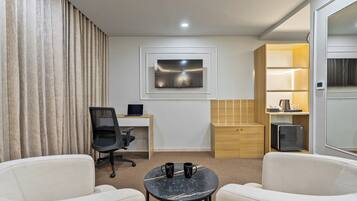 Una habitación de hotel moderna con escritorio, una silla de oficina, dos sillones, una mesita con dos tazas, un televisor montado en la pared y un minibar.
