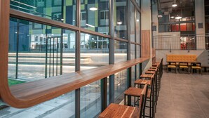 Un interior moderno con un largo banco de madera y varias mesas de madera, ventanas amplias y vistas al exterior.