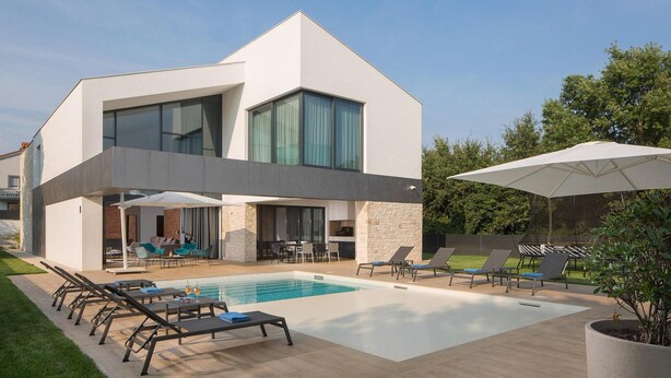 Et moderne hus i to etager med swimmingpool, udendørs møbler og en stor parasol.