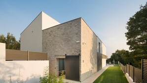 Et moderne hus med en stenvæg, et skråt tag og en lille forhave med græsplæne og grussti.